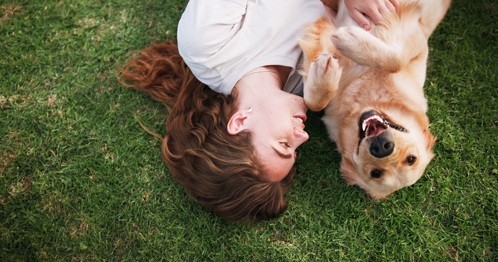 Una donna sdraiata sul prato con il cane è pronta per partire per vacanze pet friendly: con QuattrozampeTravel trovi destinazioni in tutta Italia