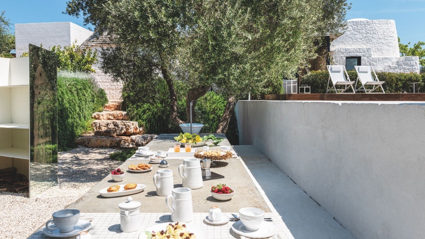 Protagonista dell'area pranzo esterna di questo trullo con piscina in Puglia è il tavolo di cemento (di 5 metri di lunghezza).
